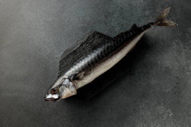 Pürüzsüz siyah bir kesme tahtasının üzerinde koyu bir arka planda füme uskumrunun göz kamaştırıcı görüntüsü. Yemek meraklıları ve menü tasarımcıları için mükemmel. Bu resim gurme deniz ürünlerinin cazibesini yakalar.