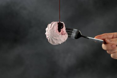 Pembe marşmelovlar bir çatalın üzerine narin bir şekilde mızraklanmış, lezzetli yoğunlaştırılmış süt serpiştirilmiş, hepsi koyu siyah bir zemine karşı hazırlanmış. Bu cezbedici görüntü tatlı ve hoşgörü karışımı sunuyor. Tatlı menüleri, yemek blogları ya da dolandırıcılık için mükemmel.