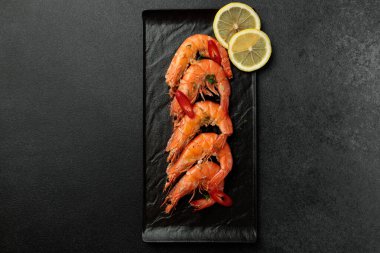 Siyah arka planda büyük pişmiş kral karidesleri. Limon dilimleri