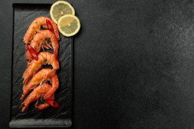 Siyah arka planda büyük pişmiş kral karidesleri. Limon dilimleri