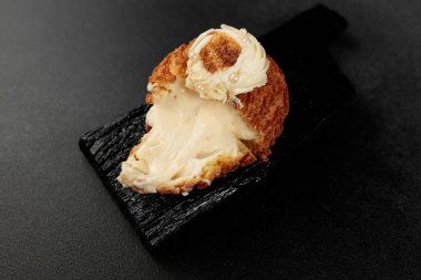 Klasik Shu keki (choux). Tereyağı ve süte dayalı muhallebi hamuru, siyah bir kesme tahtasına krema ile doldurulmuş klasik muhallebi.