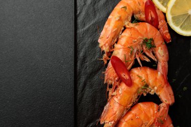 Siyah arka planda büyük pişmiş kral karidesleri. Limon dilimleri