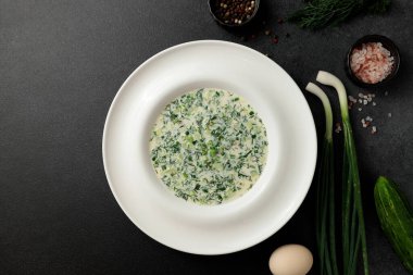 Taze salatalıklı soğuk çorba, sosis, et suyu ve ekşi krema siyah arka planda bir tabakta. Geleneksel bir yemek okroshka.