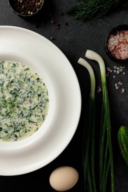 Taze salatalıklı soğuk çorba, sosis, et suyu ve ekşi krema siyah arka planda bir tabakta. Geleneksel bir yemek okroshka.