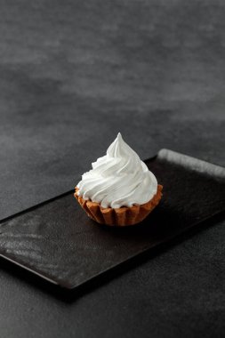 Kum sepeti yüksek protein kremiyle süslenmiş. Gri bir arka planda siyah bir tabakta duran lezzetli ve tatlı bir tatlı.