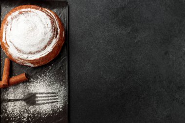 Yuvarlak, lezzetli çörek tarçınlı ve pudra şekerli gri arka planda siyah bir tabakta