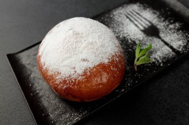 Çilekli iştah açıcı bir çörek, gri arka planda siyah dikdörtgen bir tabakta toz şeker serpiştirilmiş.