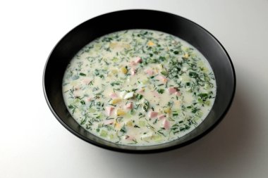 Taze salatalıklı soğuk çorba, sosis, et suyu ve ekşi krema beyaz arka planda siyah bir tabakta. Geleneksel bir yemek okroshka.