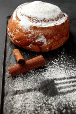 Yuvarlak, lezzetli çörek tarçınlı ve pudra şekerli gri arka planda siyah bir tabakta
