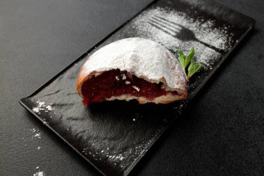 Çilekli iştah açıcı bir çörek, gri arka planda siyah dikdörtgen bir tabakta toz şeker serpiştirilmiş.