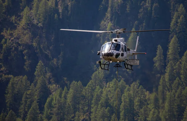 stock image Close-up of a helicopter flying over the forest with attached transportastion rope in swiss alps