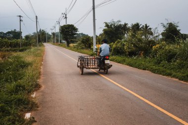 Local man riding a motorcycle with side cart on a country road in Thailand