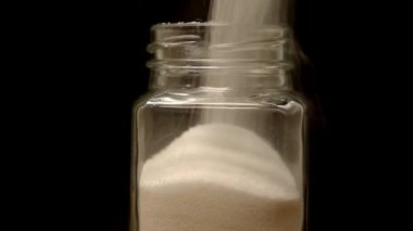 Pouring salt into the glass jar, close up against black background