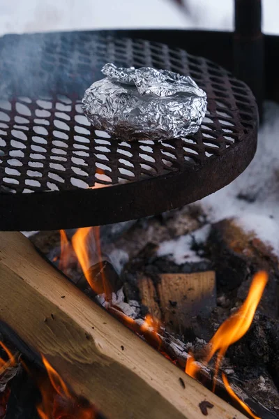 Foil wrapped food on a grill over the campfire in winter.