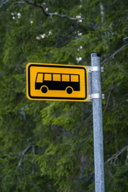 Finlandiya 'da sarı yerel otobüs durağı tabelası ve arka planda yeşil çam ağaçları.