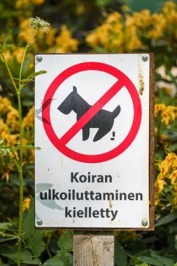 Yazılı müstehcen yazı: Fince 'de köpek gezdirmek yasaktır ve arka planda sarı çiçekler vardır..