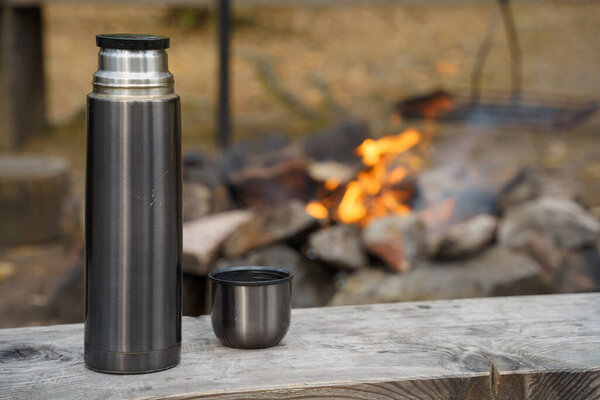 Scratched steel thermos bottle on a wooden bench next to the campfire