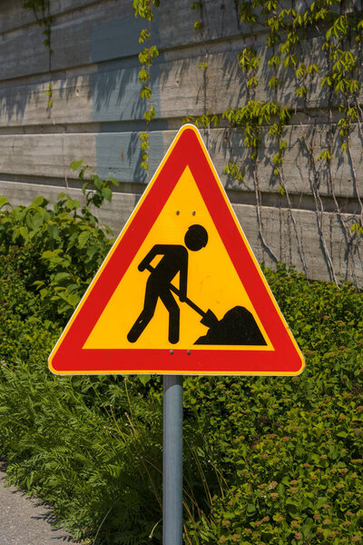 Roadworks warning sign with green bushes and a concrete wall in the background