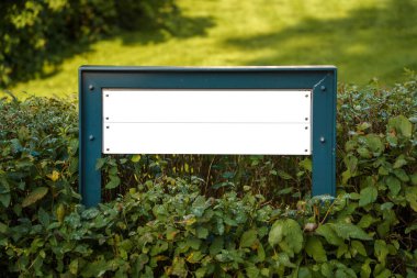 Bahçeyi çevreleyen bir çalılıkta küçük metalik beyaz bir tabela.