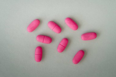 Gri yüzeyde bir grup pembe ilaç hapı, üst görünüm.