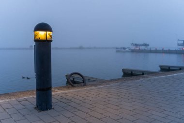 Bollard light in a harbor on a blue misty morning clipart