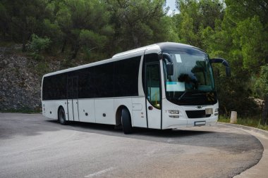 Dar virajlı bir dağ yolunda dönen beyaz turist otobüsü.