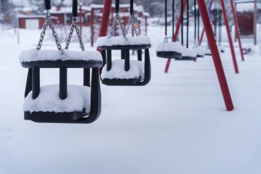 Kışın boş oyun parkında karla kaplı salıncaklara yakın. Finlandiya.