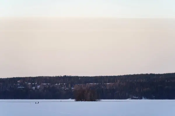 Frozen lake landscape with people ice-fishing in the distance. Lahti, Finland.