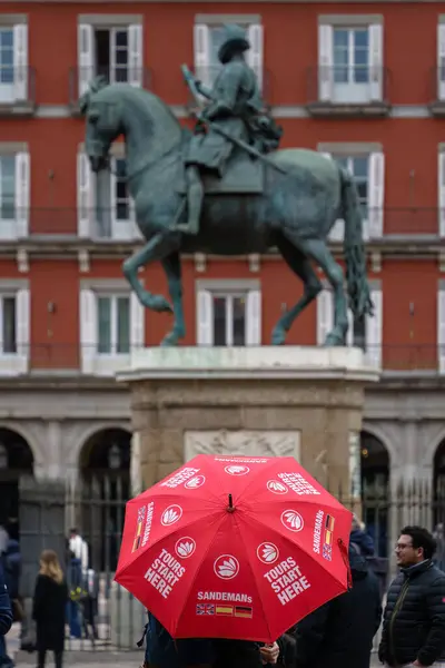 stock image Madrid, Spain. February 11, 2024 - Tour guide with red umbrella standing in Front of the equestrian statue at Plaza Mayor