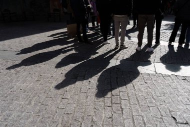 Ayakta duran bir grup insan, şehrin kaldırımlarına gölge düşürüyor..