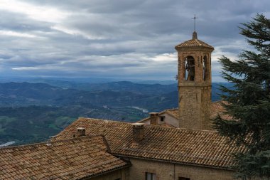 Chiesa di San Francesco 'nun tarihi çan kulesi San Marino' da bulutlu bir günde manzaralı tepe manzarasına bakar.