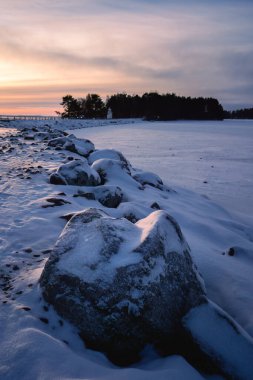 Gün batımında kıyı şeridi boyunca karla kaplı kayalar.