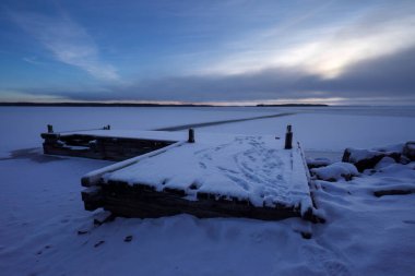 Winter landscape featuring a snow-covered dock by a frozen lake at dusk clipart