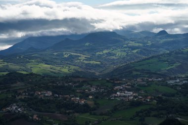 Sonbaharda bulutlu bir gökyüzünün altında uzak dağlarla San Marino kırsalında