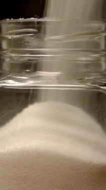 Pouring salt into the glass jar, close up against black background