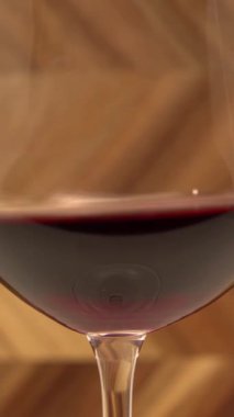 Red wine swirling in wine glass close up against wooden background.