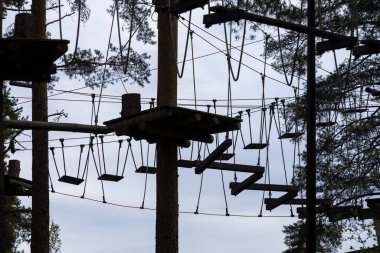 Platformlu yüksek ipler ve gökyüzüne karşı siluetlenmiş salıncaklar. Hyvinkaa, Finlandiya.