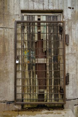 Beton duvarın arkasında eski kırık ahşap kapılı paslı çelik ızgara kapı.
