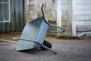 Eski bir sanayi binasının dışında bir el arabası yan yatar..