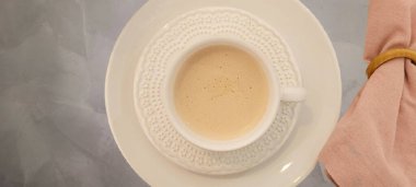 Gri arka planlı kahvaltı masası, beyaz fincan ve beyaz çay tabağı