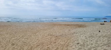 Güneşli bir günde kumsalın beyaz kumlu ve sakin denizi sahile vuran yüzücüler ve sörfçülerle.