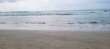 Güneşli bir günde kumsalın beyaz kumlu ve sakin denizi sahile vuran yüzücüler ve sörfçülerle.