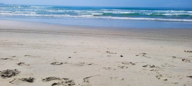 Güneşli bir günde kumsalın beyaz kumlu ve sakin denizi sahile vuran yüzücüler ve sörfçülerle.