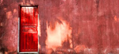 Kırmızı kapısı ve kırsal duvarı olan eski bir ev.