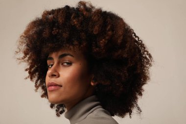 Afro saçlı, gülümseyen ve beyaz arka plandaki kameraya bakan genç bir kadın. Yüksek kalite fotoğraf.