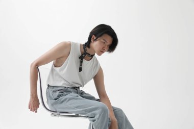 Beyaz duvarın üzerinde oturan kendine güvenen ve şık Asyalı genç adam. Yatay olarak. Yüksek kalite fotoğraf.