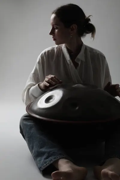 Woman plays relaxing music with hang drum handpan posing on white background. High quality photo.