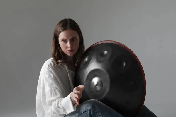 Woman plays relaxing music with hang drum handpan posing on white background. High quality photo.