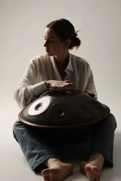 Woman plays relaxing music with hang drum hand-pan posing indoor. Vertical. High quality photo.