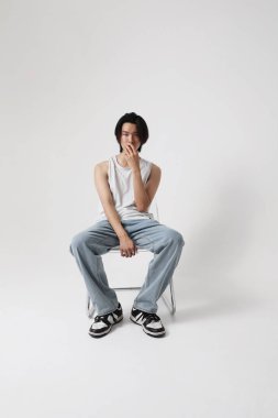 Beyaz arka planda oturan kendine güvenen Asyalı genç adamın dikey portresi. Yüksek kalite fotoğraf.